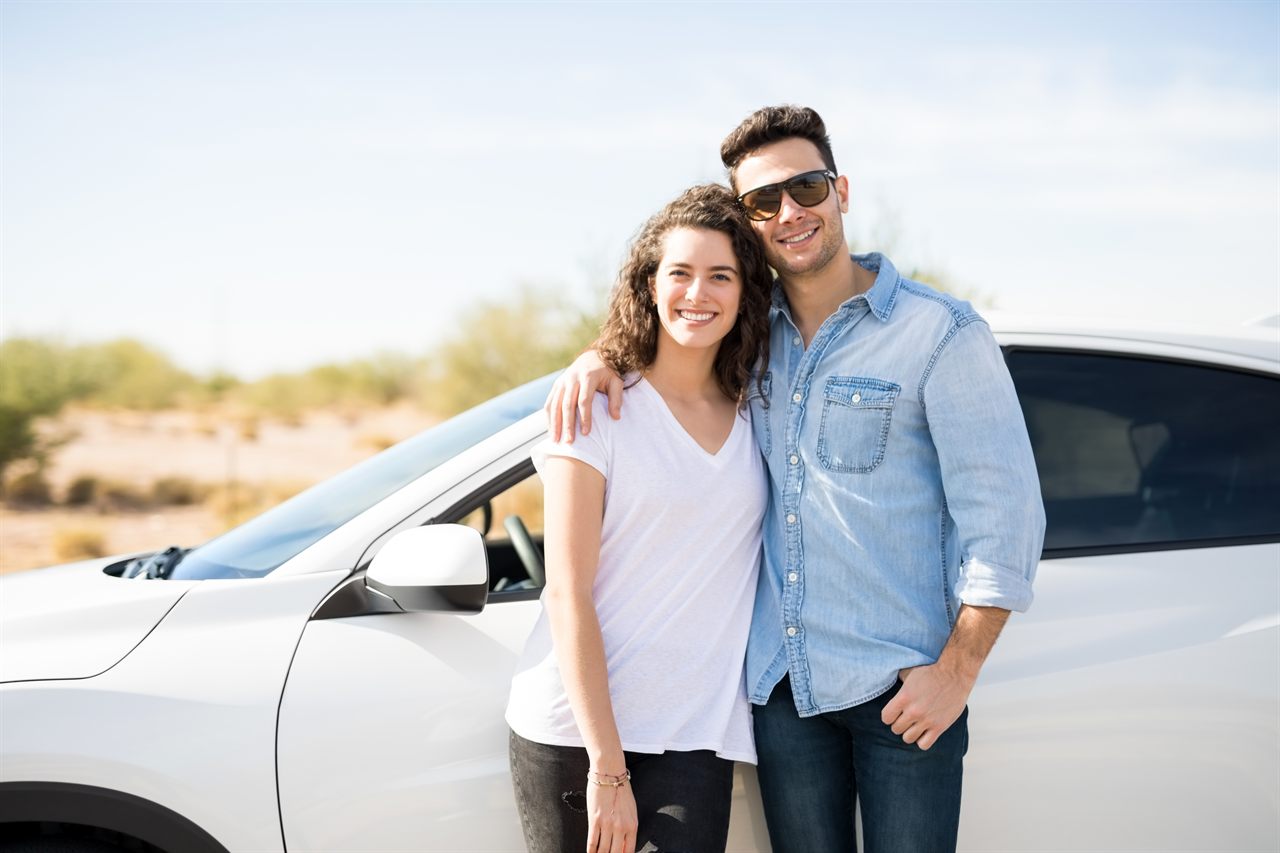 Jeune couple souriant à côté de sa première voiture, illustrant l'assurance auto jeune conducteur